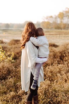 a woman holding a child in her arms while walking through a field with tall grass