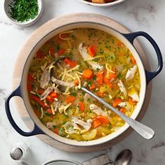 a pot filled with chicken noodle soup next to a bowl of bread and parsley