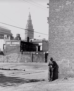 black and white photograph of man leaning against brick wall