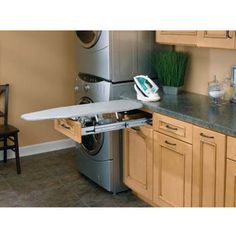 an ironing board is sitting on top of a dryer in a kitchen with wooden cabinets