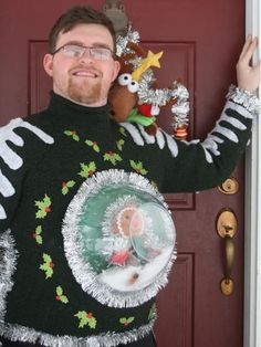 a man in a ugly christmas sweater is holding up a glass ornament and smiling at the camera