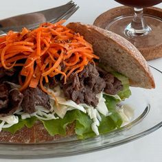 a sandwich with meat, lettuce and carrots on it next to a glass of wine