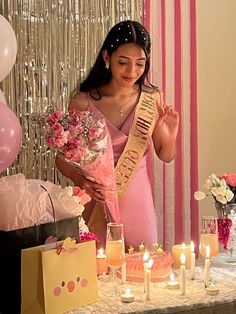 a woman in a pink dress holding a bouquet and standing next to a table with candles