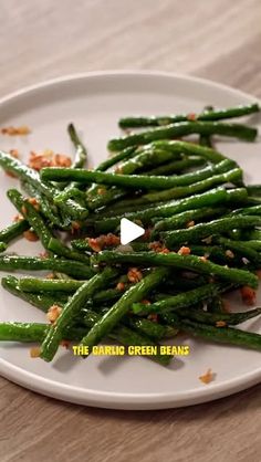 a white plate topped with green beans covered in seasoning on top of a wooden table