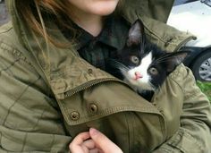 a woman is holding a black and white cat in her arms while wearing a green jacket