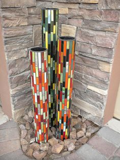 two tall colorful vases sitting in front of a stone fireplace with rocks around it