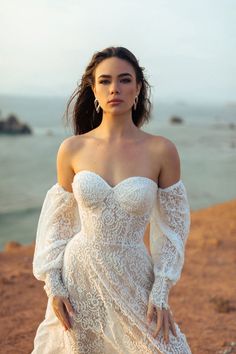 a woman in a white dress standing on the beach with her hands on her hips