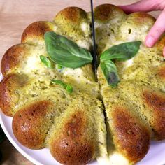 someone is cutting into a pizza on a white plate with green leaves and cheese toppings