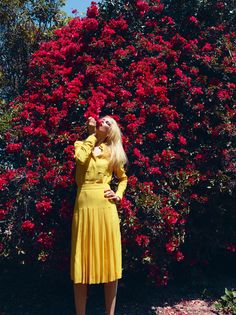 a woman standing in front of a bush with red flowers on it's side