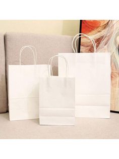 two white paper bags sitting on top of a couch next to a painting in the background