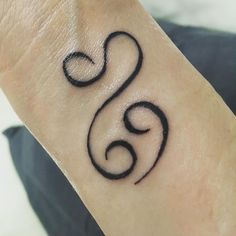 a small black tattoo on the wrist of a person's hand, with swirls