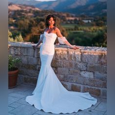 a woman in a white dress leaning on a stone wall