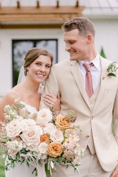 a bride and groom standing in front of a white house with flowers on their bouquets