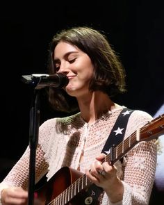 a woman holding a guitar and singing into a microphone at a music concert with an american flag on her shirt