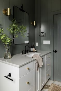 a bathroom with gray walls and white counter tops, gold handles, brass fixtures and a plant in a glass vase on the vanity