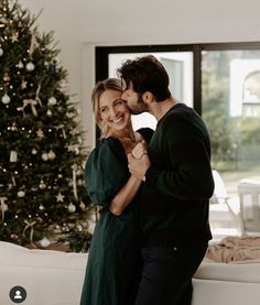 a man and woman kissing in front of a christmas tree