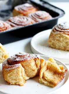 two white plates topped with pastries next to a baking pan filled with powdered sugar