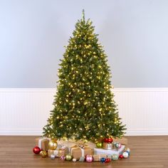 a christmas tree with presents under it on the floor in front of a white wall