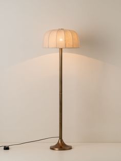 a floor lamp with a white shade on the base and a black cord plugged into it