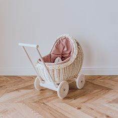 a wicker baby stroller with pink blanket in it on the floor next to a white wall