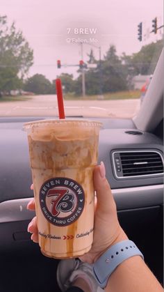 a person holding up a cup of coffee in their hand while sitting in a car