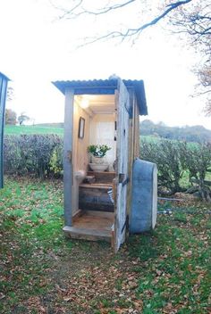 an outhouse in the middle of a field with its door open and some plants growing inside