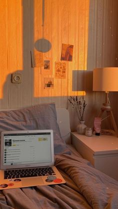 a laptop computer sitting on top of a bed next to a night stand and lamp