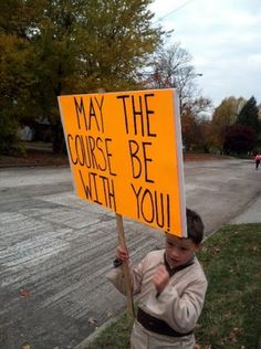 a young boy holding a sign that says may the course be with you