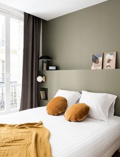 a bed with two pillows on top of it in front of a window next to a lamp