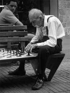 an old man playing chess with another man sitting on a bench