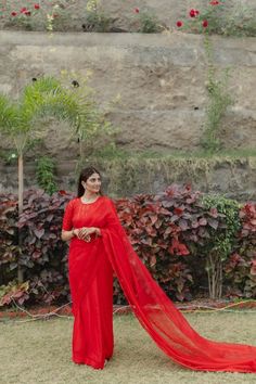 a woman wearing a red sari standing in front of some bushes