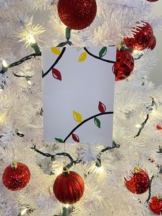 a white christmas tree with red ornaments and a card hanging from it's side