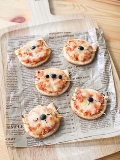 four small pizzas with cheese and black olives on them are sitting on a newspaper