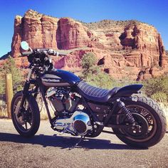 a black motorcycle parked in front of a mountain with red rocks behind it and a blue sky