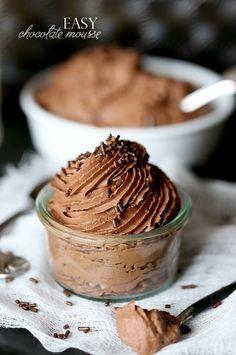 two bowls filled with chocolate pudding on top of a white cloth next to spoons