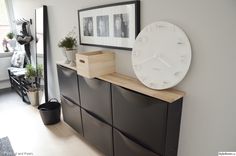 a white clock mounted to the side of a wall next to a black cabinet with drawers