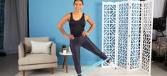 a woman standing in front of a blue wall with her hands on her hips and arms behind her back