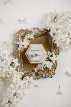 two wedding rings sitting on top of a mirror surrounded by white flowers