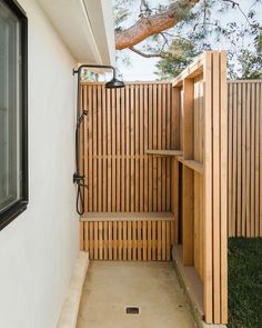 an outdoor shower with wooden slats on the outside wall and grass in the yard