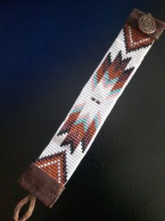 a brown and white beaded wristband with a button on the clasp that is attached to a black surface