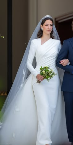 the bride is walking down the aisle with her bouquet in hand and wearing a white gown