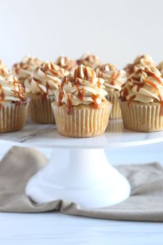 several cupcakes with caramel drizzle and frosting on a white cake plate