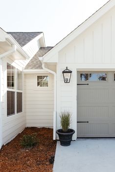 a white house with a gray garage door and two plants in the front yard area