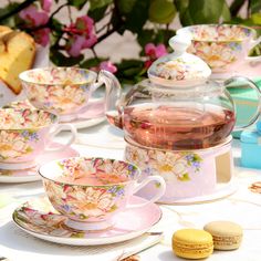 there are many tea cups and saucers on the table with flowers in front of them