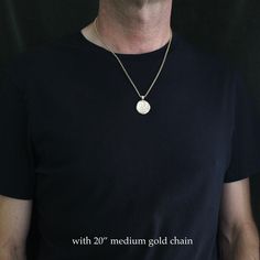 a man wearing a black t - shirt with a white disc pendant on his neck