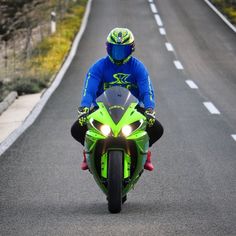 a man riding on the back of a green motorcycle down a curvy road