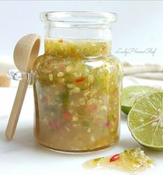 a glass jar filled with food next to limes and a wooden spoon on a white surface