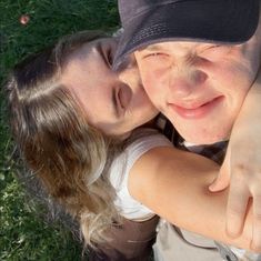 a man and woman laying on the grass with their arms around each other, giving thumbs up