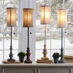 three lamps sitting on top of a table next to a window with snow outside it