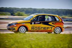 an orange and black car driving on a race track with grass in the foreground